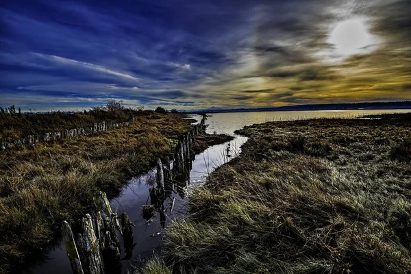 Wunderschöne Landschaft der Gezeitensumpfe zwischen trockenen Grasfeldern unter dem atemberaubenden Himmel bei Sonnenuntergang — Stockfoto