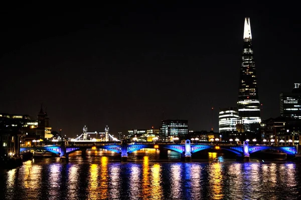 Красивый снимок освещенного моста вдоль реки и города на тёмном фоне — стоковое фото