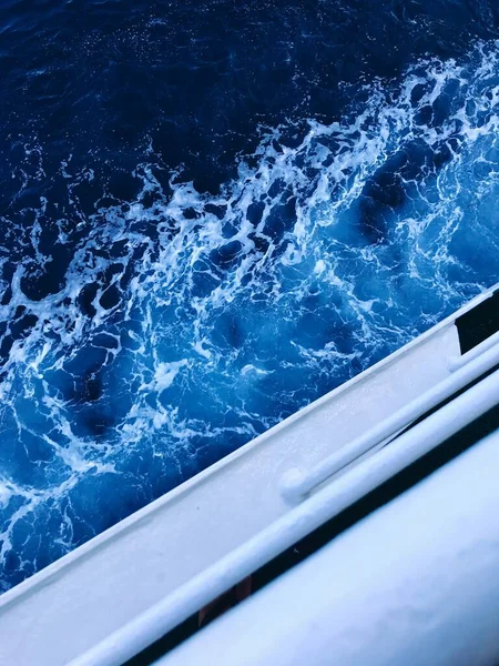 A vertical shot of the foamy waves of the ocean taken from a sailing boat