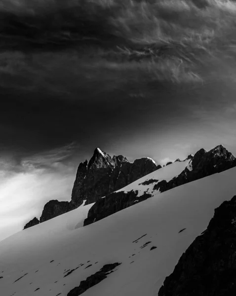 Grayscale baixo ângulo tiro rochas nevadas sob o céu com enormes nuvens cinzentas no inverno — Fotografia de Stock