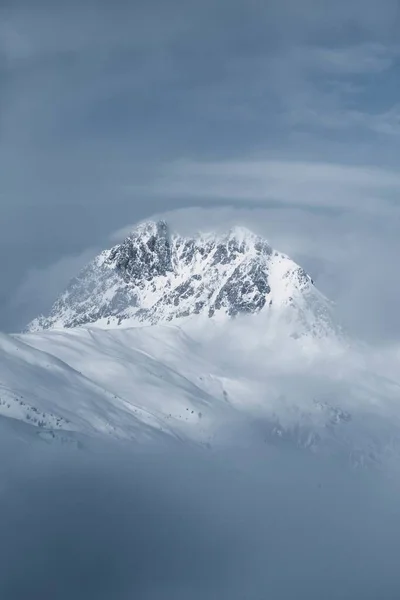 Vertical shot of a beautiful rocky hill covered with snow enveloped in fog — Stock Photo, Image