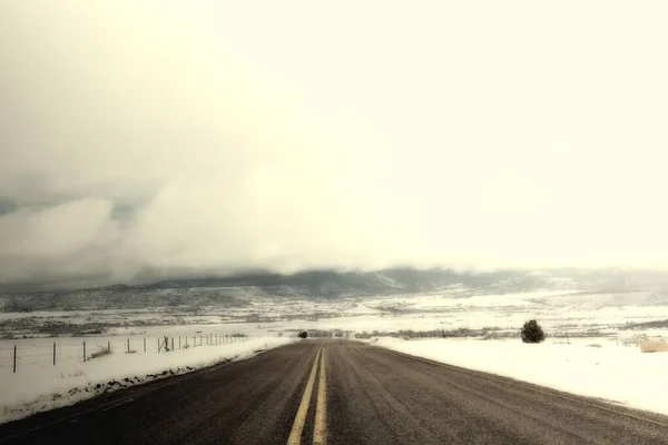 Belo tiro de uma estrada no centro de um vale coberto de neve sob o céu nebuloso branco — Fotografia de Stock