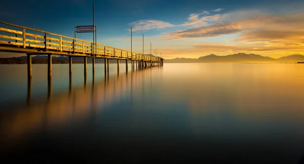 Verschwommene Reflexion des schönen Sonnenaufgangs am Himmel und der Seebrücke im ruhigen blauen Meer — Stockfoto