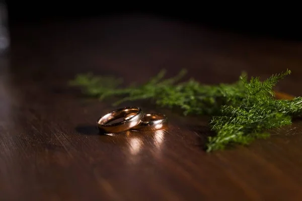 Közelkép arany jegygyűrűkről egy fából készült asztalon fenyőlevelek közelében. — Stock Fotó