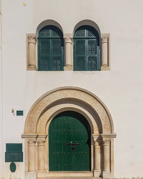 Vertikální záběr budovy se zelenými okny ve tvaru oblouku a dveřmi na bílé stěně — Stock fotografie