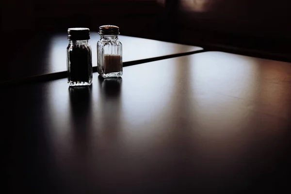 Agitadores de sal y pimienta en la mesa en la oscuridad con rayos de sol cayendo dentro —  Fotos de Stock