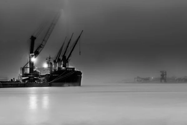 Captura a escala de grises de un barco industrial con luces en el mar envueltas en niebla — Foto de Stock