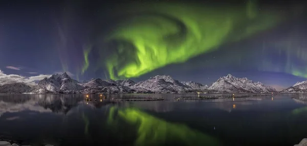 Wide shot of the reflection of the auroras in a lake surrounded by snow covered hills in Norway