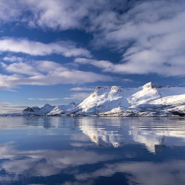 Reflejo de un acantilado cubierto de nieve en el agua bajo las hermosas nubes en el cielo en Noruega — Foto de Stock