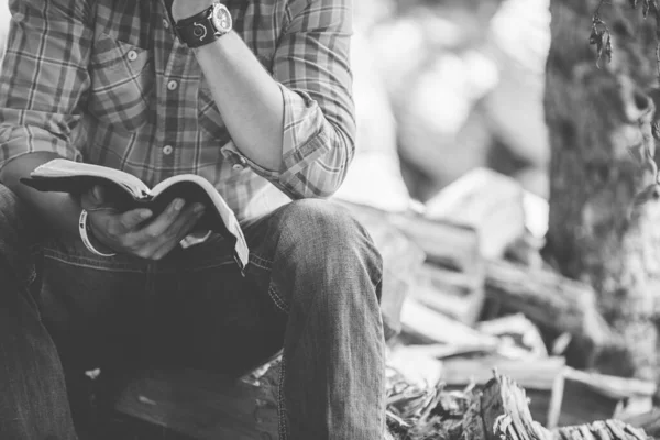 Nahaufnahme eines auf dem Boden sitzenden Mannes beim Lesen der Bibel mit verschwommenem Hintergrund — Stockfoto