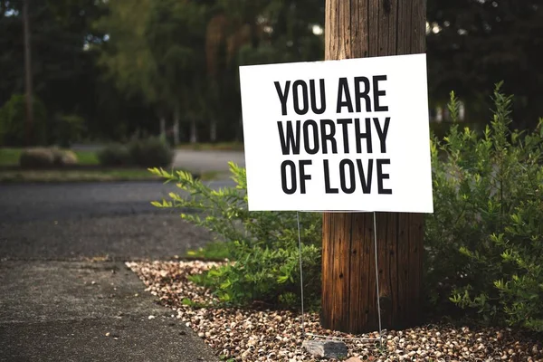 Nahaufnahme von Ihnen sind der Liebe wert Beschilderung vor einem Baumstamm in der Nähe der Straße — Stockfoto