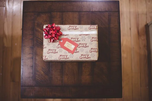 Nad głową ujęcie prezentu świątecznego z czerwoną kokardą na drewnianym stole — Zdjęcie stockowe