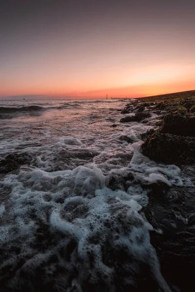 Вертикальний Знімок Пінистих Хвиль Моря Виходять Берег Дивовижним Заходом Сонця — стокове фото