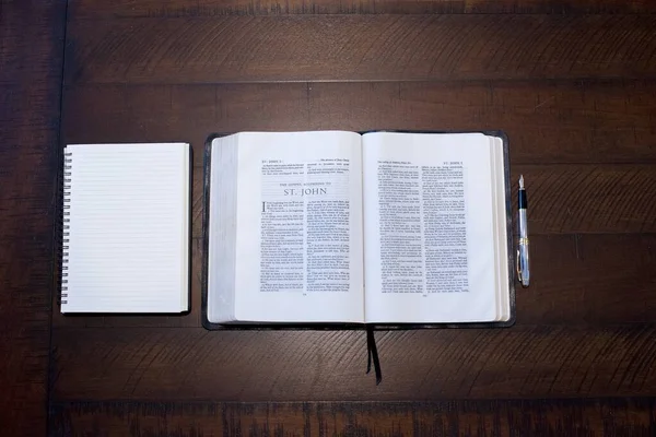 Împușcat deasupra capului unei Biblii deschise în mijlocul unui carnețel și a unui stilou pe o suprafață de lemn — Fotografie, imagine de stoc