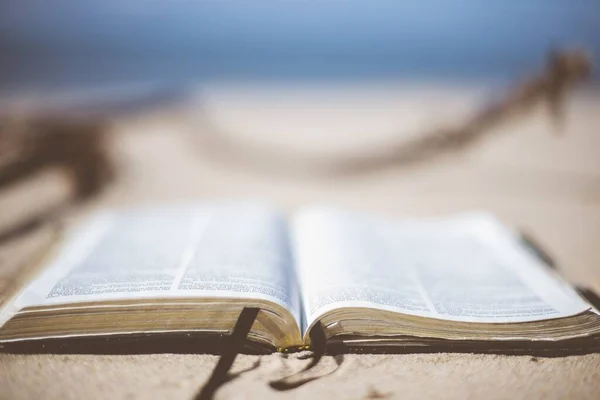 Close-up opname van een open bijbel op een zandige ondergrond bij het strand met een wazige achtergrond — Stockfoto