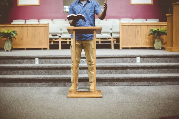 Homme debout en lisant la bible près d'un stand en bois avec un fond flou — Photo