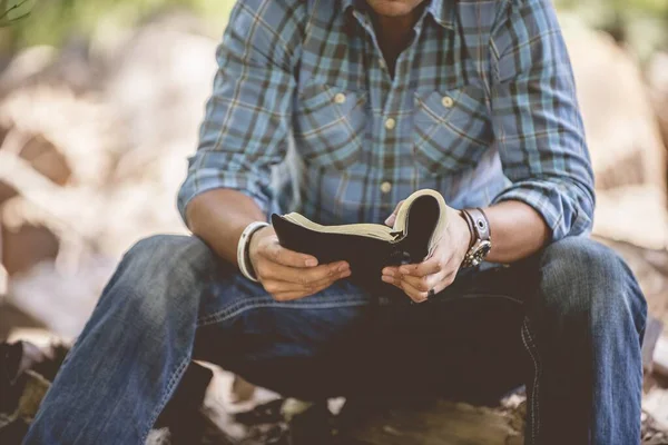 Detailní záběr muže v neformálním oblečení, jak čte Bibli svatou na rozmazaném pozadí — Stock fotografie