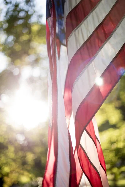 Vertical closeup shot of the united states flag with the sun shining in the background