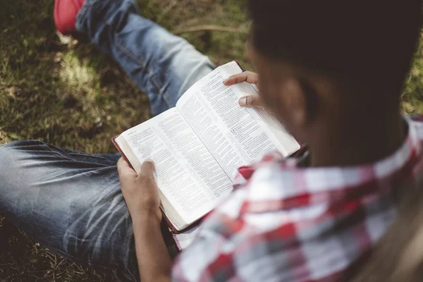 Kopfschuss eines Mannes, der sich beim Lesen der Bibel mit verschwommenem Hintergrund gegen den Baum lehnt — Stockfoto