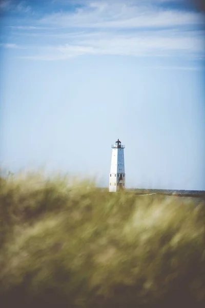 Vertical selective focus shot of a lighthouse in the distance with a blue sky in the background — Stockfoto