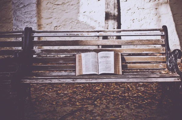 Közelkép egy nyitott bibliáról egy homályos hátterű fa padon — Stock Fotó
