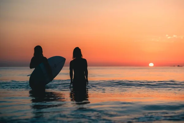 2019年6月29日 息をのむような夕日を眺めながら水の中に立つ2人のサーファーの美しいショット — ストック写真