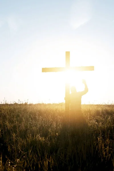 Вертикальный Снимок Мужчины Стоящего Возле Деревянного Креста Поднятой Рукой Сияющим — стоковое фото