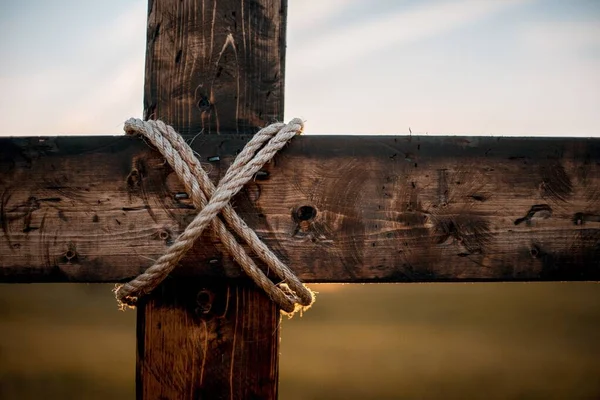 Closeup shot of a wooden cross with a rope wrapped around and a blurred background — Stock Photo, Image