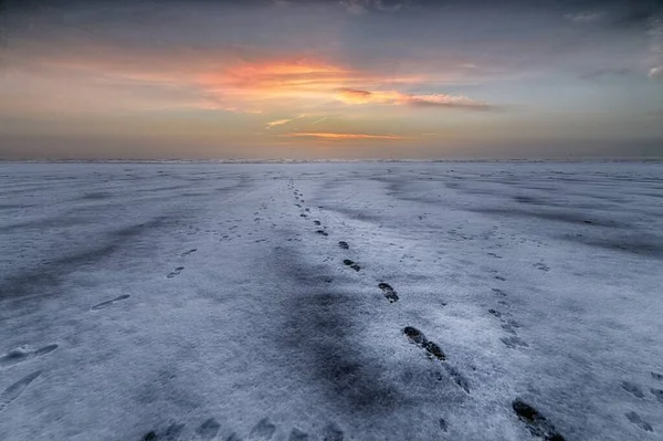 Belo tiro de pôr do sol sobre a praia com pegadas que levam ao mar — Fotografia de Stock