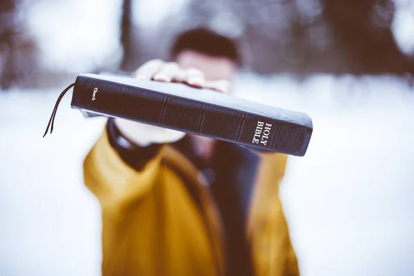 Primer plano de un macho sosteniendo la Biblia hacia la cámara con un fondo borroso —  Fotos de Stock