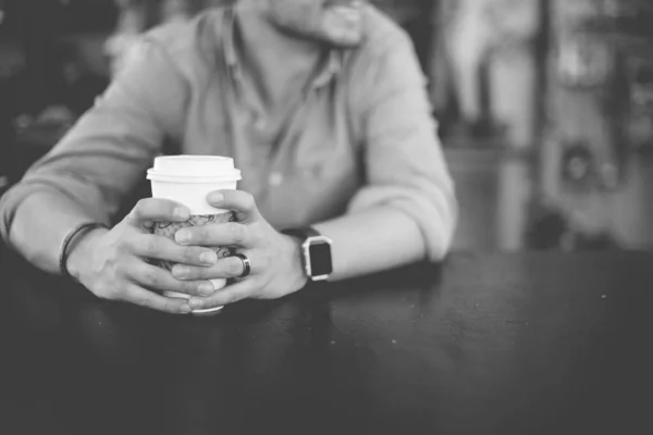 Gros plan d'un mâle tenant son café assis avec un fond flou en noir et blanc — Photo