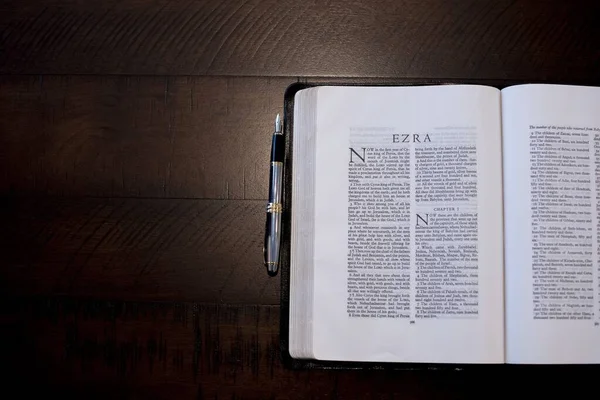 Overhead shot of an open Bible near a fountain pen on a wood surface — Stok Foto