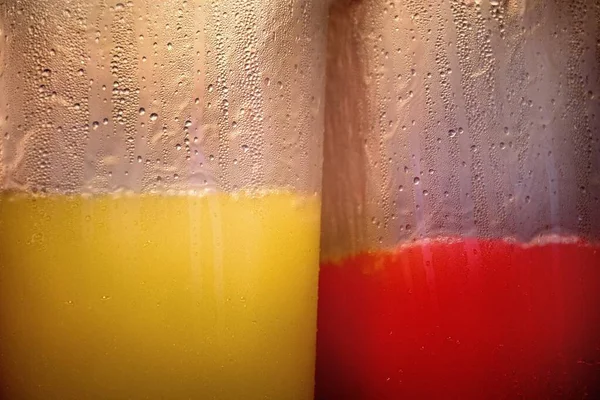 Szekrénykép pohár tele piros és sárga italok - nagy hűvös háttér — Stock Fotó