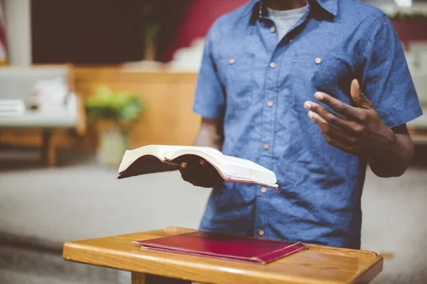 Primer plano de un hombre leyendo la Biblia cerca de un soporte de madera con un fondo borroso — Foto de Stock