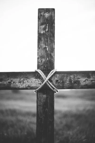 背景がぼやけている木の十字架の周りに巻かれたロープの垂直グレースケールショット。 — ストック写真