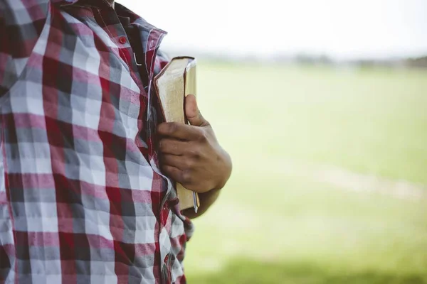 Primer plano de un macho sosteniendo la Biblia contra su pecho con un fondo borroso — Foto de Stock