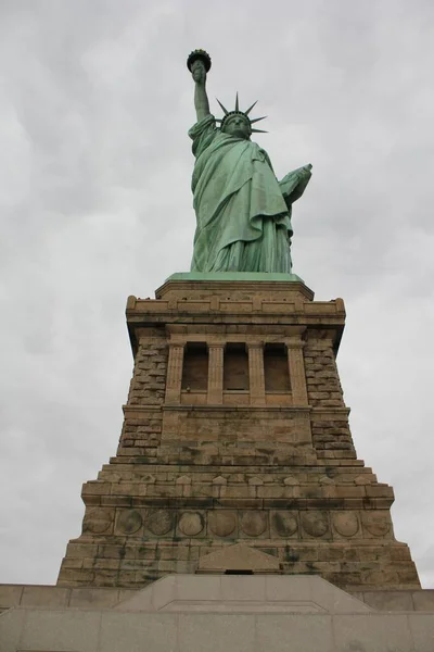 Vertical baixo ângulo tiro da Estátua da Liberdade, em Nova York, com um céu nublado no fundo — Fotografia de Stock