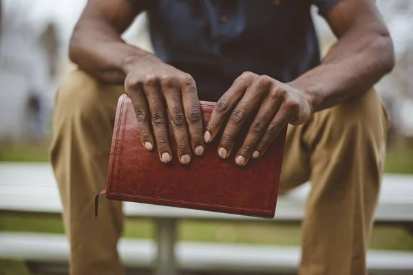Primer plano de un hombre sentado en el parque mientras sostiene la Biblia con un fondo borroso — Foto de Stock