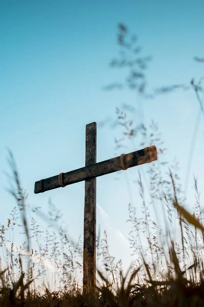 Tiro vertical de ángulo bajo de una cruz de madera hecha a mano en un campo herboso con un cielo azul en el fondo — Foto de Stock