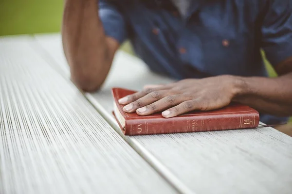 Detailní záběr muže s rukou na bibli na dřevěném stole s rozmazaným pozadím — Stock fotografie