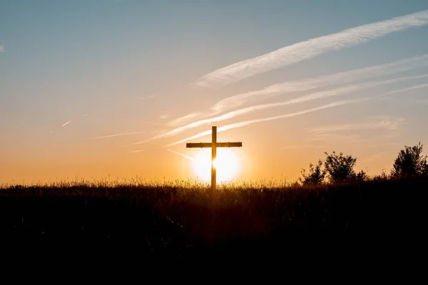 Sylwetka krzyża w trawiastym polu z promieniującym słońcem w tle — Zdjęcie stockowe