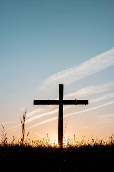 Sylwetka drewnianego krzyża w trawiastym polu z niebieskim niebem w tle w ujęciu pionowym — Zdjęcie stockowe