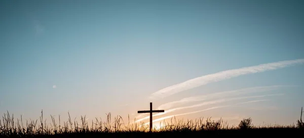O largo tiro de uma mão fez uma cruz de madeira em um campo gramado com um céu azul no fundo — Fotografia de Stock
