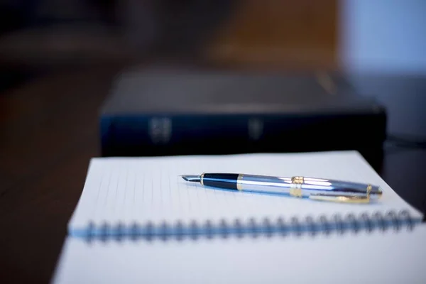 Closeup tiro de uma caneta-tinteiro em um caderno com uma bíblia borrada no fundo — Fotografia de Stock