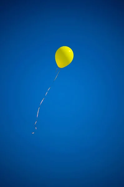 Tiro vertical de um balão amarelo no ar com um céu azul no fundo — Fotografia de Stock