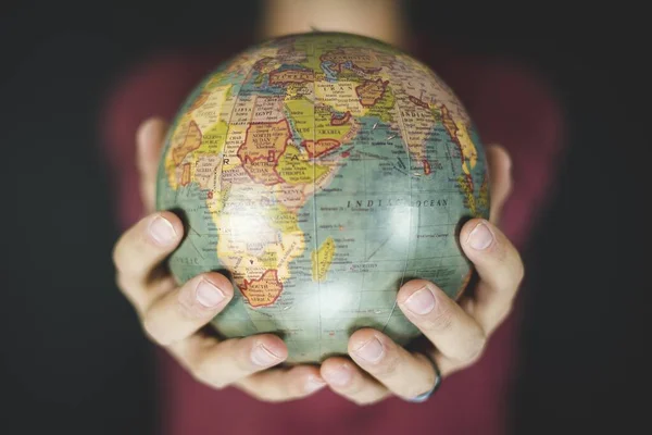 Closeup shot of a person holding a small globe with two hands and a blurred background