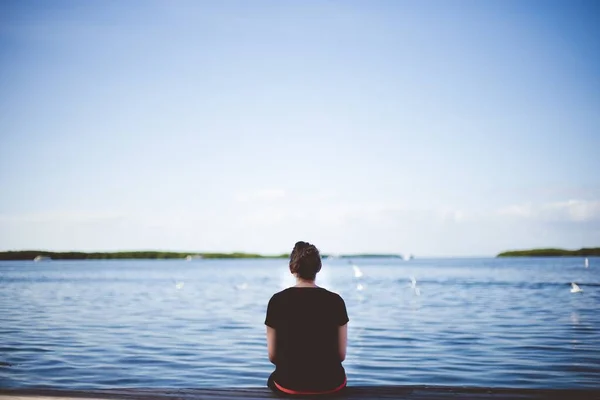 Vrouw zitten in de buurt van de zee en kijken in de verte schot van achteren met een wazige achtergrond — Stockfoto