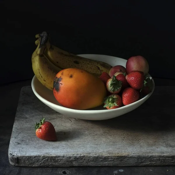 Νεκρή ζωή φωτογραφία των νωπών φρούτων σε ένα λευκό πιάτο σε μαύρο φόντο — Φωτογραφία Αρχείου