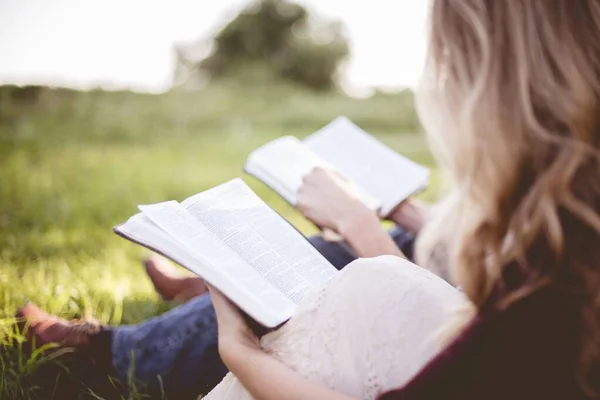 Nahaufnahme von zwei Personen, die auf einer Wiese sitzen und die Bibel mit verschwommenem Hintergrund neu interpretieren — Stockfoto