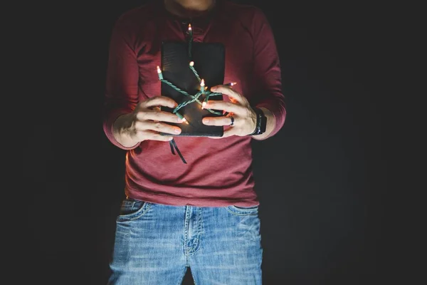 Close-up tiro de uma pessoa segurando a bíblia com luzes iluminadas envolto em torno dele e fundo preto — Fotografia de Stock